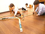 木製のレールと列車で線路をつなぎ、見立て遊びを楽しむ幼児クラスの子どもたち"